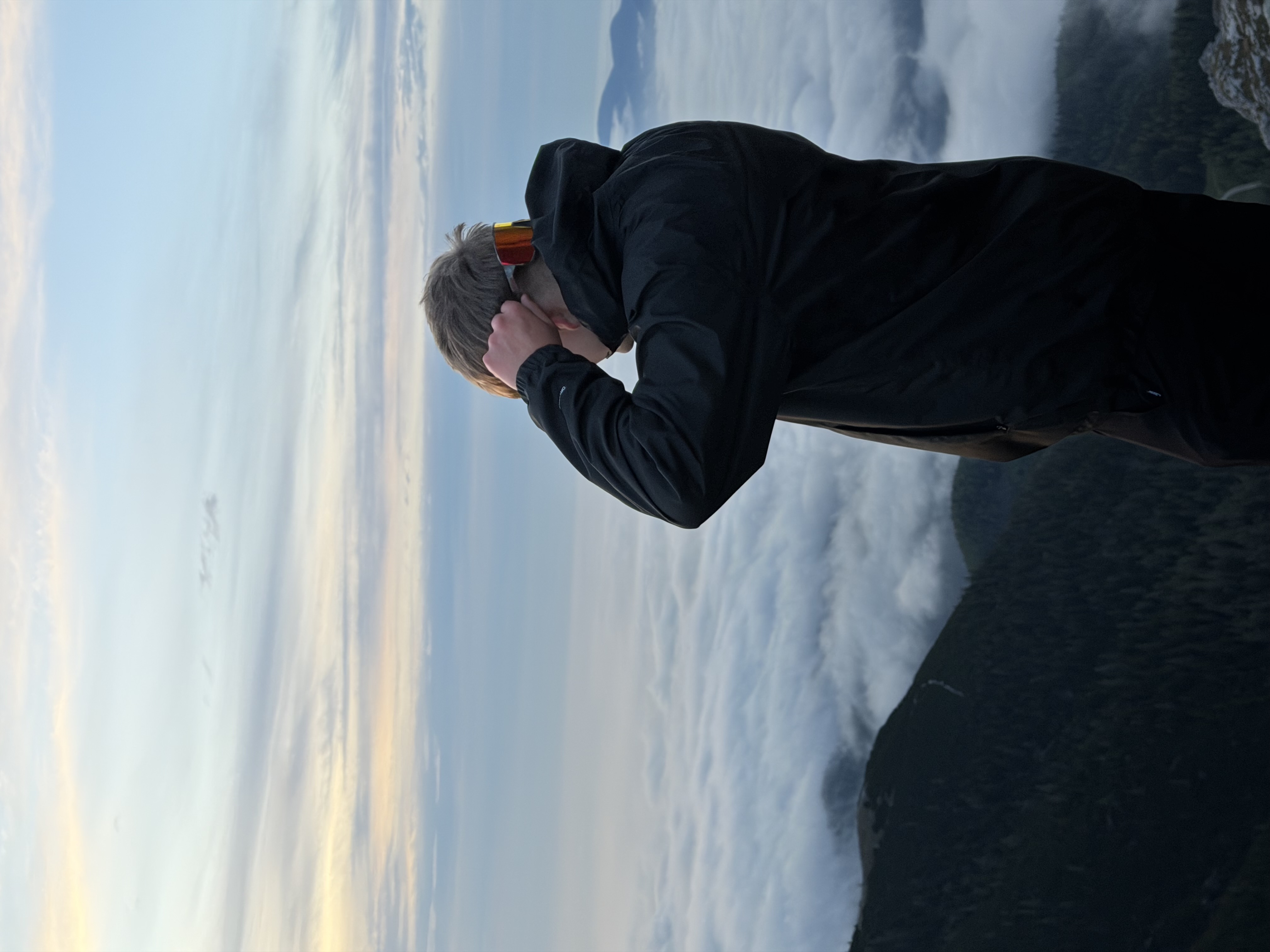 Felix Gollnhuber seen from behind on a summit, above a sea of clouds at dawn